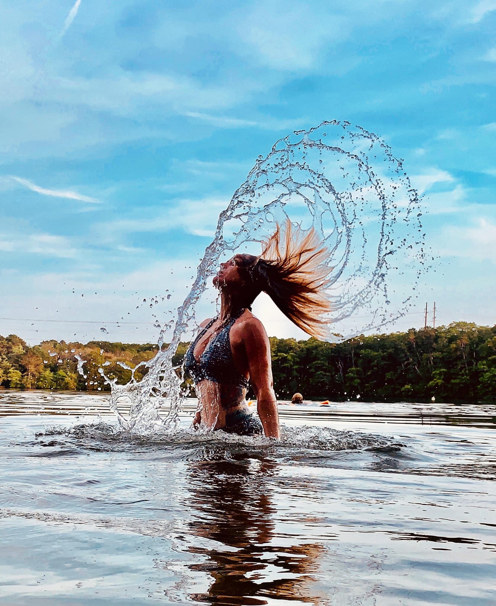woman standing in water throwing her wet hair back with water splashing over her head